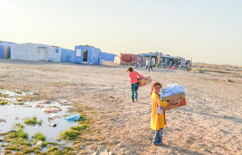 Young children carry boxes of aid back to their home in the camp